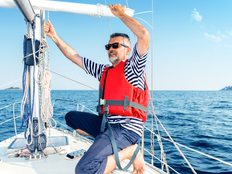 A man out on his boat enjoying the ocean, wearing a safety life jacket