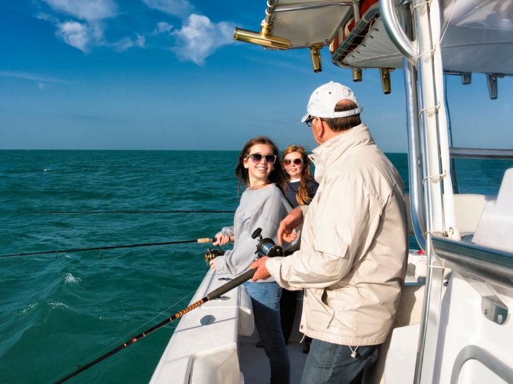 Family fishing off the the side of their boat, all standing comfortably