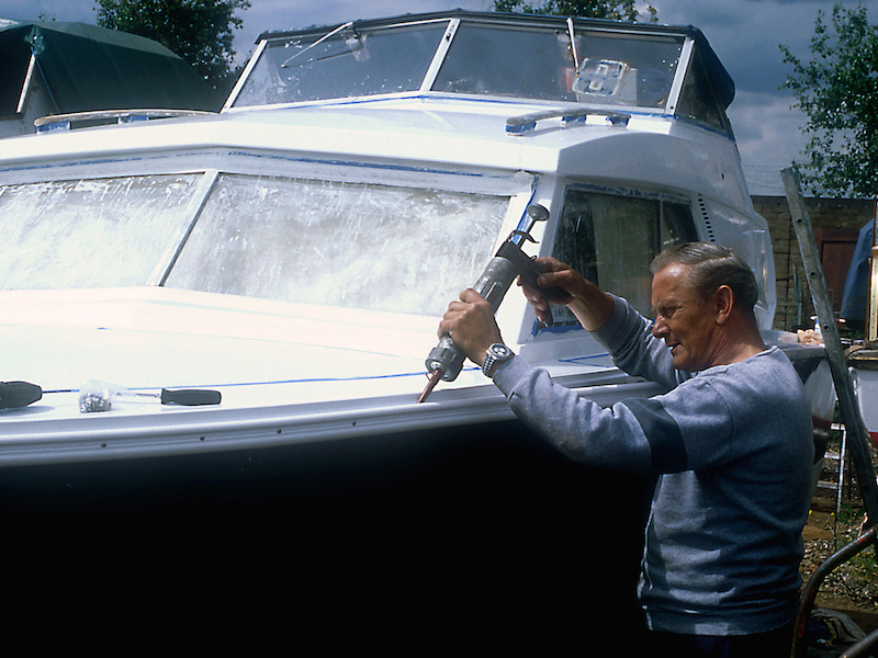 A man applying sealant to the front of his boat.